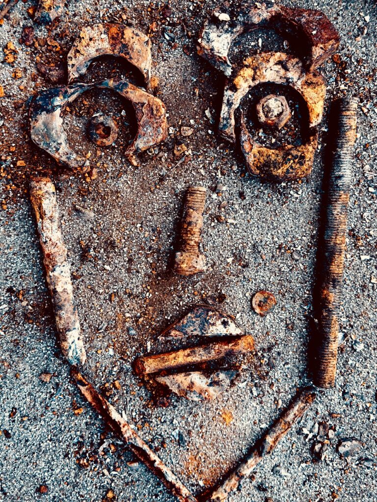 Artistic face made from rusty metal pieces on gravel background.